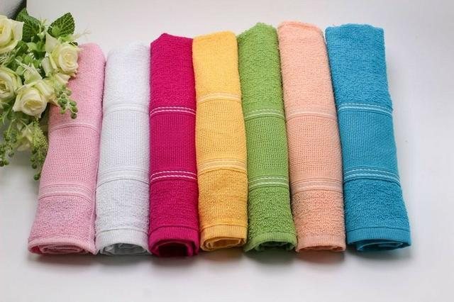 Imagem ilustrativa de toalhas de mão  Toalhas de mão coloridas e dobradas com uma flor ao lado - Divulgação