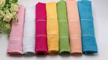 Imagem ilustrativa de toalhas de mão  Toalhas de mão coloridas e dobradas com uma flor ao lado - Divulgação