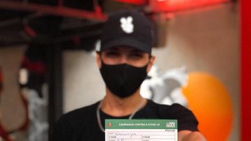 Quem apresentar o comprovante de vacinação ganha uma porção batata-frita na faixa Hamburgueria de Santos oferece batata-frita de graça para quem apresentar comprovante de vacinação Jovem usando máscara e mostrando o comprovante de vacinação para a câmera - Reprodução/Redes sociais