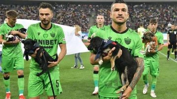 Cachorros entraram com bandanas com seus nomes para que o telespectador identificasse o animal e adotasse o do seu agrado Time tem ideia criativa para incentivar adoção de cachorros Atletas do futebol romeno com cachorros no colo - Reprodução/Twitter