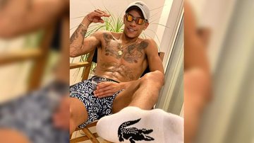 MC Paulin da Capital alegou que produção desconhecia regras sobre circulação de vans no município MC Paulin da Capital cancela show ao ser impedido de entrar em Bertioga Artista sentado sem camisa com óculos de sol e boné e um copo na mão - Divulgação