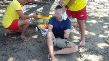 Turista sofre queda em pedras de praia em Ilhabela  Turista ferido no chão com dois salva vidas ao lado - Reprodução