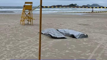Gari herói tentou salvar turista do mar revolto mas não resistiu e ambos faleceram afogados  Dois corpos na areia, cobertos com sacos - Reprodução/Guaru.TV