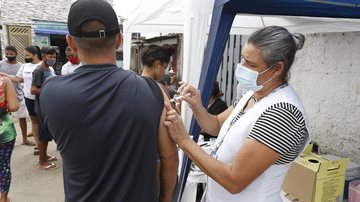 Ação acontecerá em horário diferenciado para atingir o público que faz a travessia Guarujá/Santos Estação das Barcas recebe 10° Mutirão de Natal nesta quinta (16) em Guarujá Enfermeira aplicando vacina em braço de homem que está de costas - Prefeitura de Guarujá