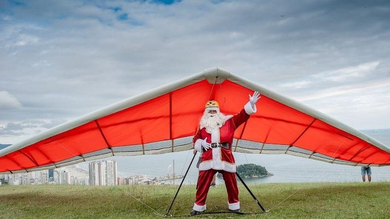 Bom velhinho sobre de teleférico e salta de parapente junto com a Mamãe Noel Trenó é coisa do passado: Papai Noel voa de parapente Foto de homem vestido de Papei Noel fazendo pose preso ao parapente - Divulgação