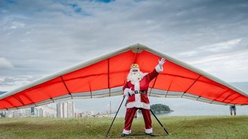 Bom velhinho sobre de teleférico e salta de parapente junto com a Mamãe Noel Trenó é coisa do passado: Papai Noel voa de parapente Foto de homem vestido de Papei Noel fazendo pose preso ao  parapente - Divulgação