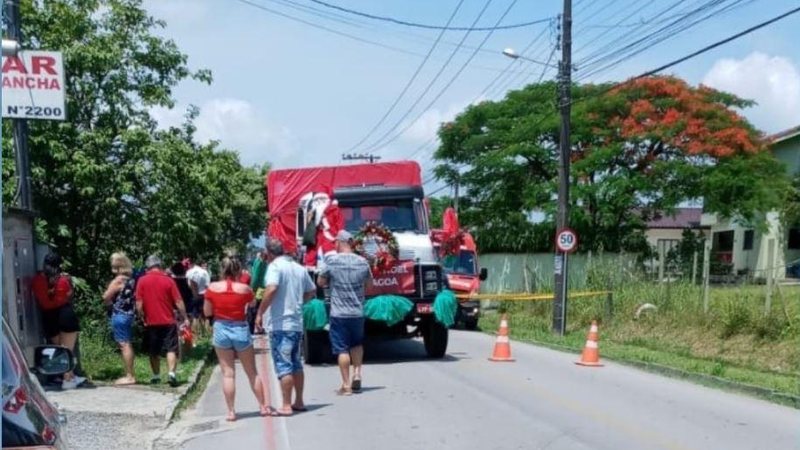 Acidente aconteceu durante carreta de Natal; idoso não suportou os ferimentos Papai Noel cai de caminhão e morre atropelado Caminhão parado e rua interditada, com pessoas em volta e uma ambulância ao fundo - Divulgação