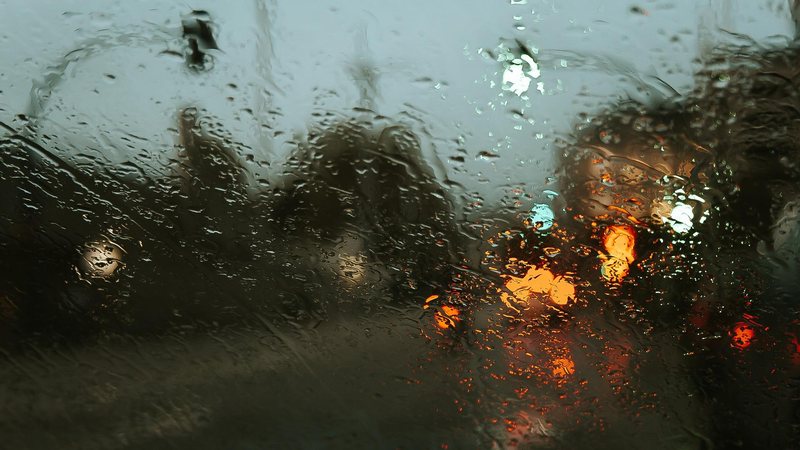 Defesa Civil de São Paulo alerta para grandes volumes de chuva, com raios e vento Defesa Civil emite alerta para chuvas fortes no litoral de São Paulo Vidro molhado de chuva com cenário de rua com luzes acesas e céu nublado atrás - Pixabay