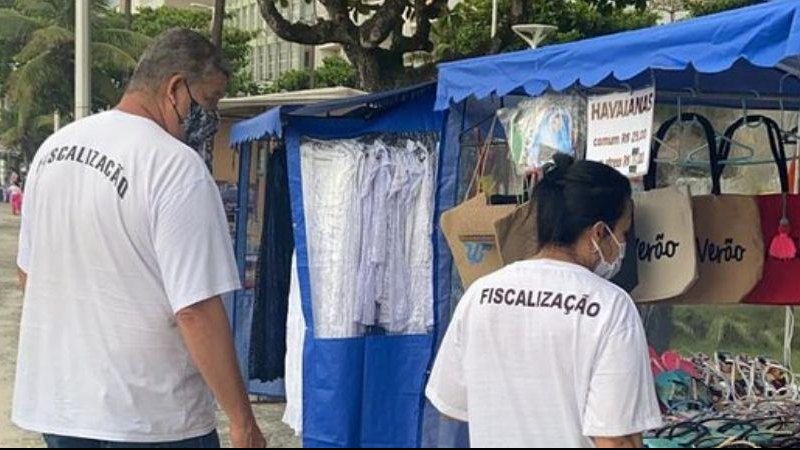 Mais de 170 pessoas trabalham para manter a segurança e a ordem na cidade Guarujá reforça esquema de segurança durante a temporada Dois fiscais analisando uma feira de artesanto - Divulgação