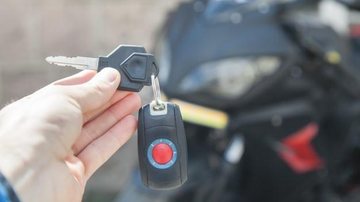 Mulher pediu a moto emprestada para dar uma volta na região e não apareceu mais Moto Pessoa com a chave de uma moto em primeiro plano e o veículo atrás - Imagem Ilustrativa