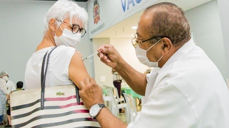 Munícipe deve levar um documento com foto e uma carteirinha de vacinação Vacinação em São Vicente Homem vacinando uma mulher em São Vicente - Divulgação
