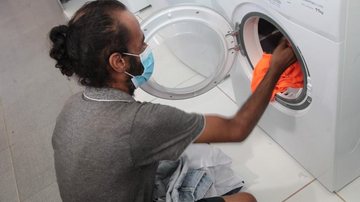 Local oferece três tanques de roupa, duas máquinas de lavar, duas secadoras, sabão em pó e em pedra, além de amaciante Santos oferece lavanderia comunitária para pessoas em situação de rua Homem coloca roupas em máquina de lavar com abertura frontal - Rogério Bomfim/Prefeitura de Santos