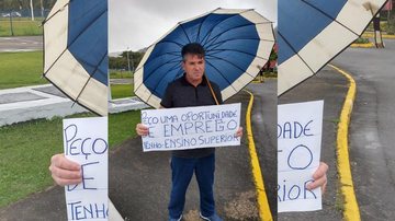 Rogério com seu cartaz em frente ao Litoral Plaza Shopping em Praia Grande Rogério Homem com cartaz pedindo emprego e um guarda-chuva nas mãos - Arquivo Pessoal