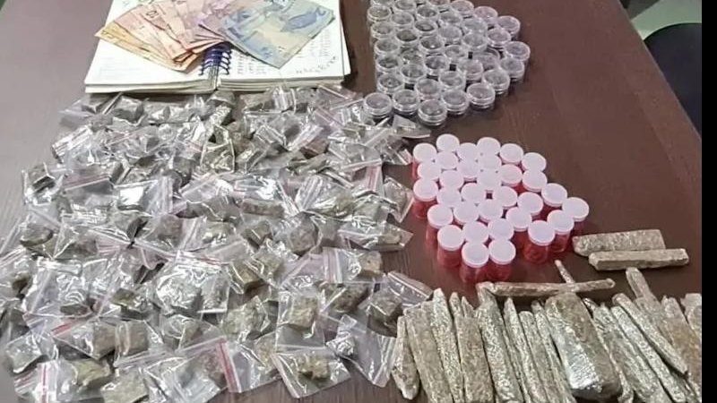 Drogas e dinheiro foram levados para a delegacia do município Drogas apreendidas Dinheiro e drogas em cima de uma mesa marrom - Divulgação