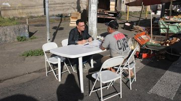 Barraca da prefeitura na feira livre do Macuco Homem sendo atendido por agente público em barraca na feira - Imagem: Divulgação / Nathália Felipe / Prefeitura de Santos