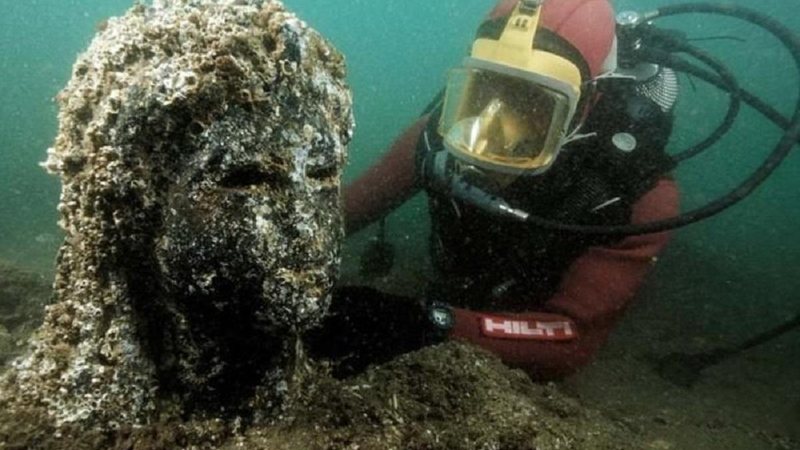 Arqueólogos encontram estátuas, esculturas e um templo também no fundo do mar Cidade no fundo do mar Pesquisador e nadador no fundo do mar ao lado de uma escultura - Divulgação