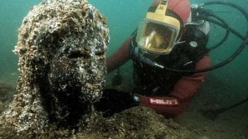 Arqueólogos encontram estátuas, esculturas e um templo também no fundo do mar Cidade no fundo do mar Pesquisador e nadador no fundo do mar ao lado de uma escultura - Divulgação