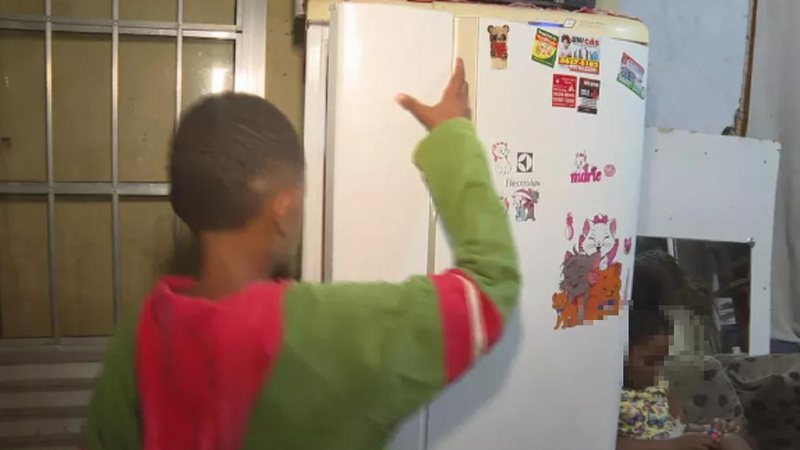 Menino de 11 anos abrindo a geladeira de casa, após ligar para o 190 e pedir por ajuda Criança com fome Criança abrindo a geladeira - Reprodução