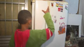Menino de 11 anos abrindo a geladeira de casa, após ligar para o 190 e pedir por ajuda Criança com fome Criança abrindo a geladeira - Reprodução