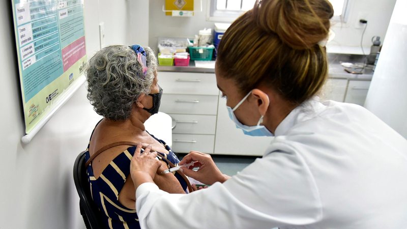 No sábado, moradores do Casqueiro terão a oportunidade de se imunizar APLICAÇÃO DE VACINA Profissional de saúde aplica uma injeção no braço de uma idosa - Prefeitura Municipal de Cubatão