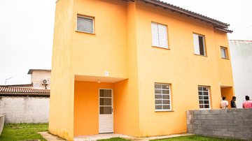As ruas do residencial estão pavimentadas e contam com passeios públicos e paisagismo Prefeitura de Bertioga e CDHU entregam últimas casas de conjunto habitacional em Vicente de Carvalho Casa amarela com pessoas entrando - Divulgação/Prefeitura de Bertioga