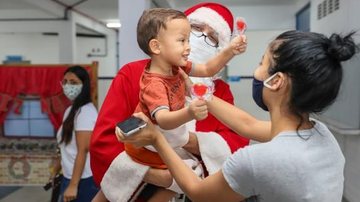 Papai Noel e seus ajudantes recebem os turistas e moradores da cidade das 17h às 22 horas, por ordem de chegada Papai Noel de Praia Grande Papai Noel com uma criança no colo - Divulgação