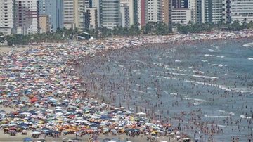 Praia Grande no Ano-Novo de 2017 Praia Grande ganha 19 novos habitantes por dia há doze anos, aponta IBGE Praia lotada de pessoas - Imagem: Reprodução / Praia Grande Mil Grau