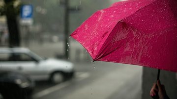 Para esta quinta-feira (1º), a probabilidade de chuva é de 70% Chuvas diminuem de intensidade nos próximos dias em Santos Pessoa segurando guarda-chuva vermelho na rua, durante chuva - Unsplash