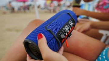 Você é #TeamSomdoMar ou #TeamMúsicaAlta? Carnaval 2023: posso usar caixas de som nas praias? Mulher segurando caixa de som portátil em praia - Félix Zucco/RBS