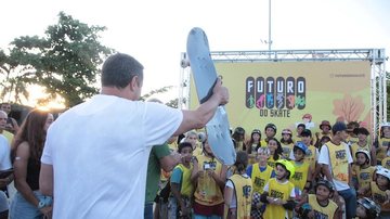O prefeito Rogério Santos esteve no emissário e prestigiou o evento ESCOLA DE SKATE II Prefeito segurando um skate e pessoas observando o momento - Comunicação Prefeitura Municipal de Santos