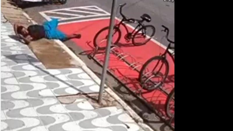 Imagens mostram o momento exato em que o homem de bermuda azul e mochila preta passa em frente ao bicicletário Homem finge cochilo na calçada para roubar bicicleta em Praia Grande Homem deitado no chão - Reprodução
