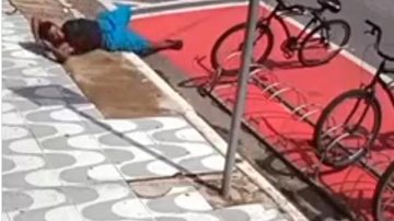 Imagens mostram o momento exato em que o homem de bermuda azul e mochila preta passa em frente ao bicicletário Homem finge cochilo na calçada para roubar bicicleta em Praia Grande Homem deitado no chão - Reprodução