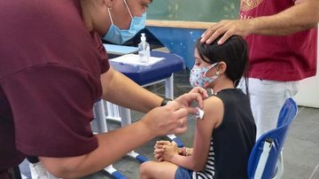 Crianças de 5 a 11 anos já podem tomar a primeira dose de reforço contra covid-19 Criança tomando vacina Criança sentada em uma cadeira e outra pessoa aplicando vacina em seu braço - Divulgação