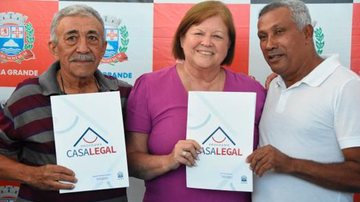 Raquel Chini com moradores contemplados com títulos do Programa Casa Legal Raquel Chini com moradores de PG Dois homens, cada um de um lado segurando um documento do Programa Casa Legal e uma mulher ruiva ao meio, prefeita da cidade - Divulgação