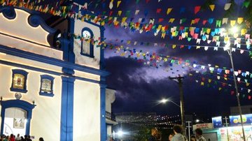 Início dos festejos é marcado pelo Fincamento do Mastro em frente a Igreja Matriz Caraguatatuba: 170ª Festa de Santo Antônio começa no domingo (28) Igreja Matriz de Santo Antônio, em Caraguatatuba, à noite, e praça enfeitada com bandeirinhas - Prefeitura de Caraguatatuba