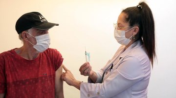 Moradores podem colocar vacinação em dia Policlínicas de Santos abrem para vacinação neste sábado Idoso sendo vacinado por enfermeira - Imagem: Divulgação / Isabela Carrari / Prefeitura de Santos
