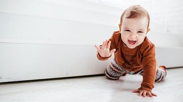 Happy child in orange sweater plays with feather on the floor - Reprodução/Freepik