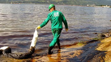 Funcionário de empresa contratada pela Transpetro aplica produto químico na praia das Cigarras, na tentativa de absorver óleo do mar - Reginaldo Pupo - 5.04.2003 / Estadão Conteúdo