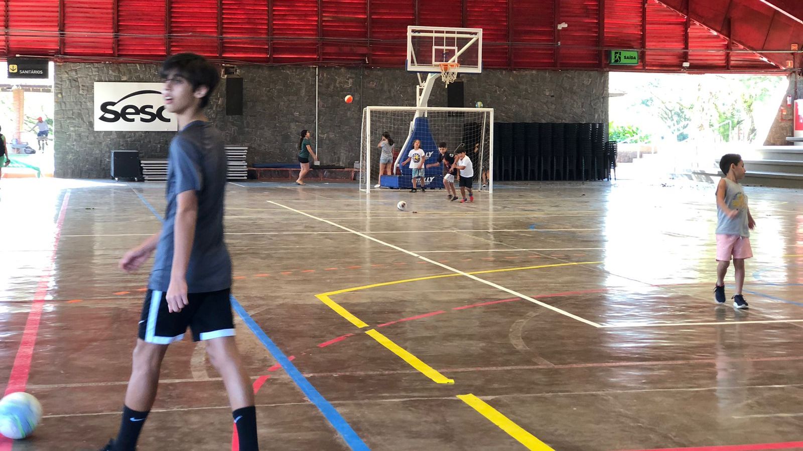 Quadra de futsal do sesc, com um menino em destaque com uma bola em seus pés